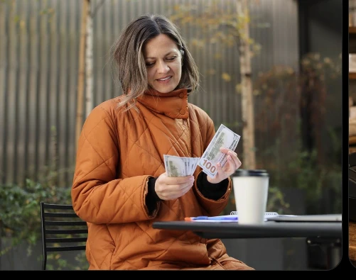 A woman counting cash while seated at an outdoor table