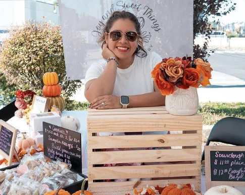 A small business owner preparing a fall market stand with pumpkins and seasonal flowers